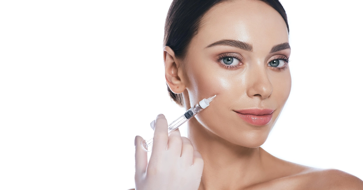 A woman holding a syringe near her cheek, wearing a glove, preparing for a Dermal Filler in Yuma, AZ cosmetic injection.